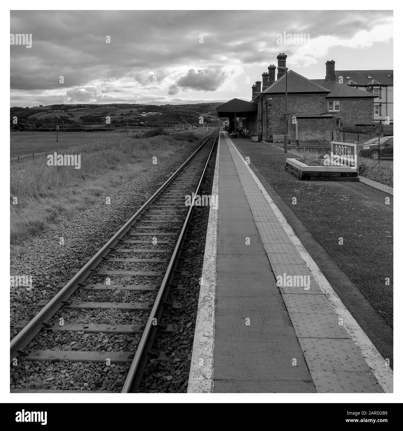 Bianco e nero [monocromatico] di una stazione ferroviaria di Borth deserta, piste che scompaiono all'orizzonte. Nuvole d'atmosfera e una cornice bianca tradizionale Foto Stock