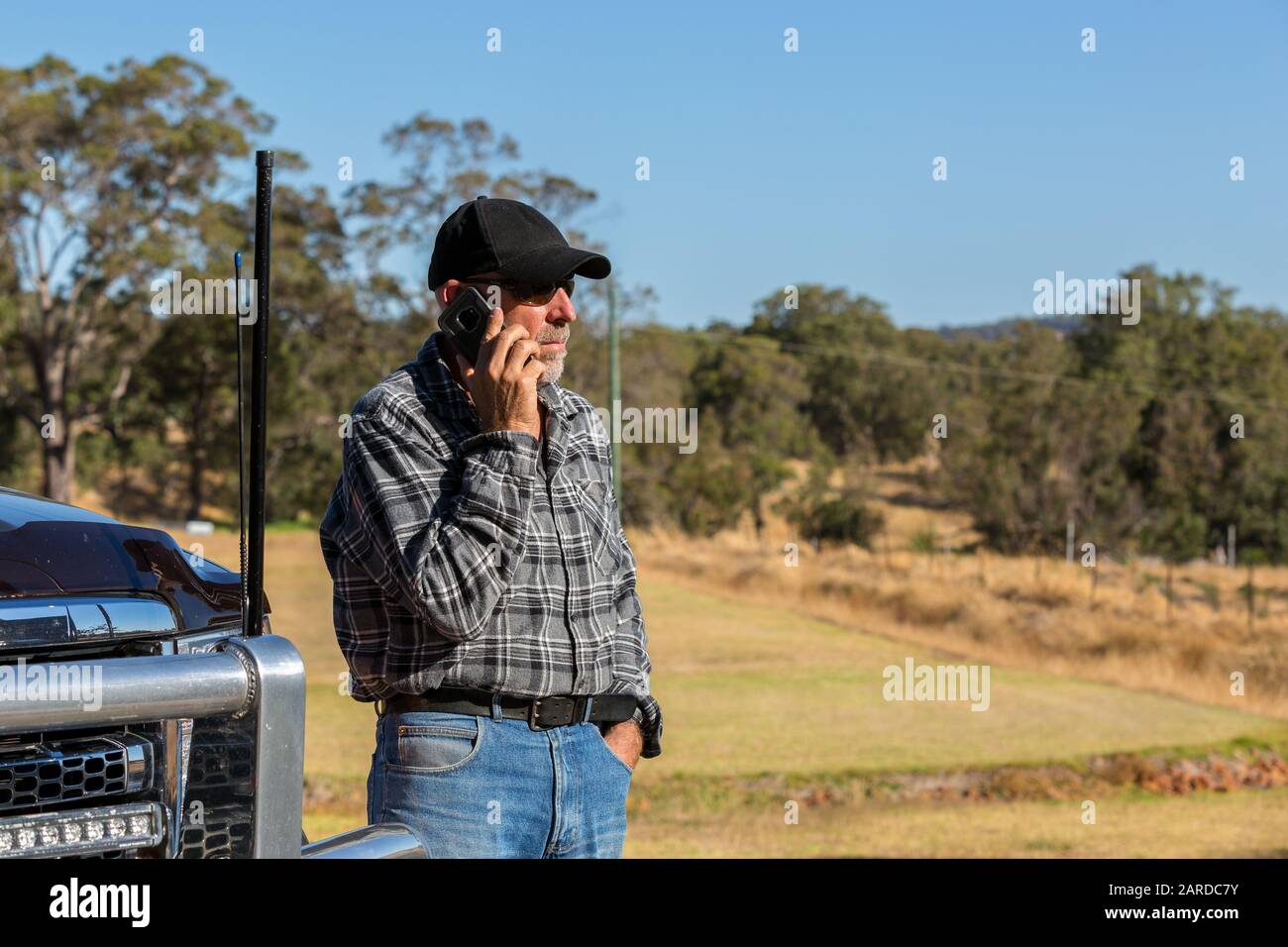 Uomo sul telefono cellulare, guardando lontano , accanto al camion con antenne. Paddock in background Foto Stock