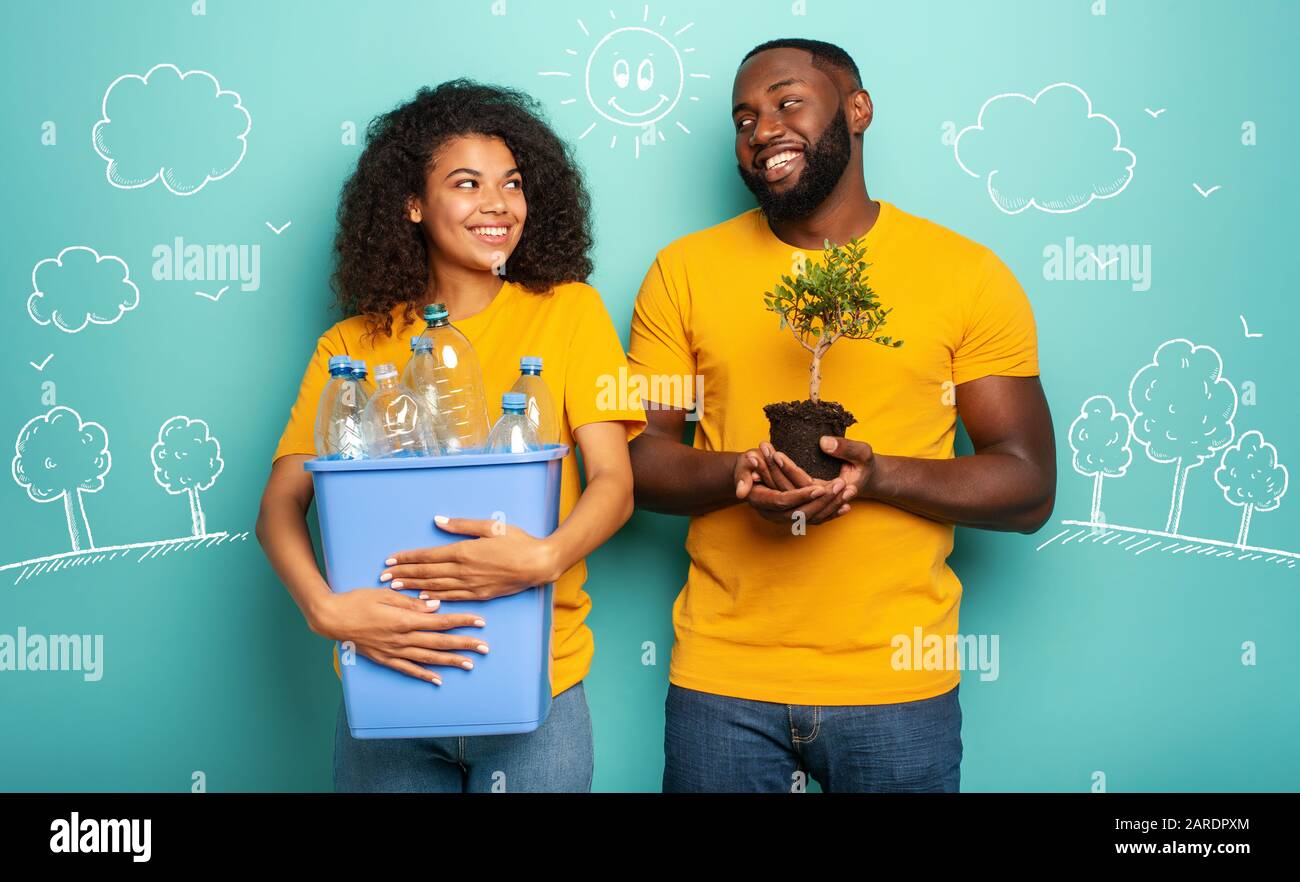 Coppia felice attesa di un contenitore in plastica con bottiglie e un piccolo albero su una luce di colore blu. Concetto di ecologia, conservazione e riciclaggio Foto Stock
