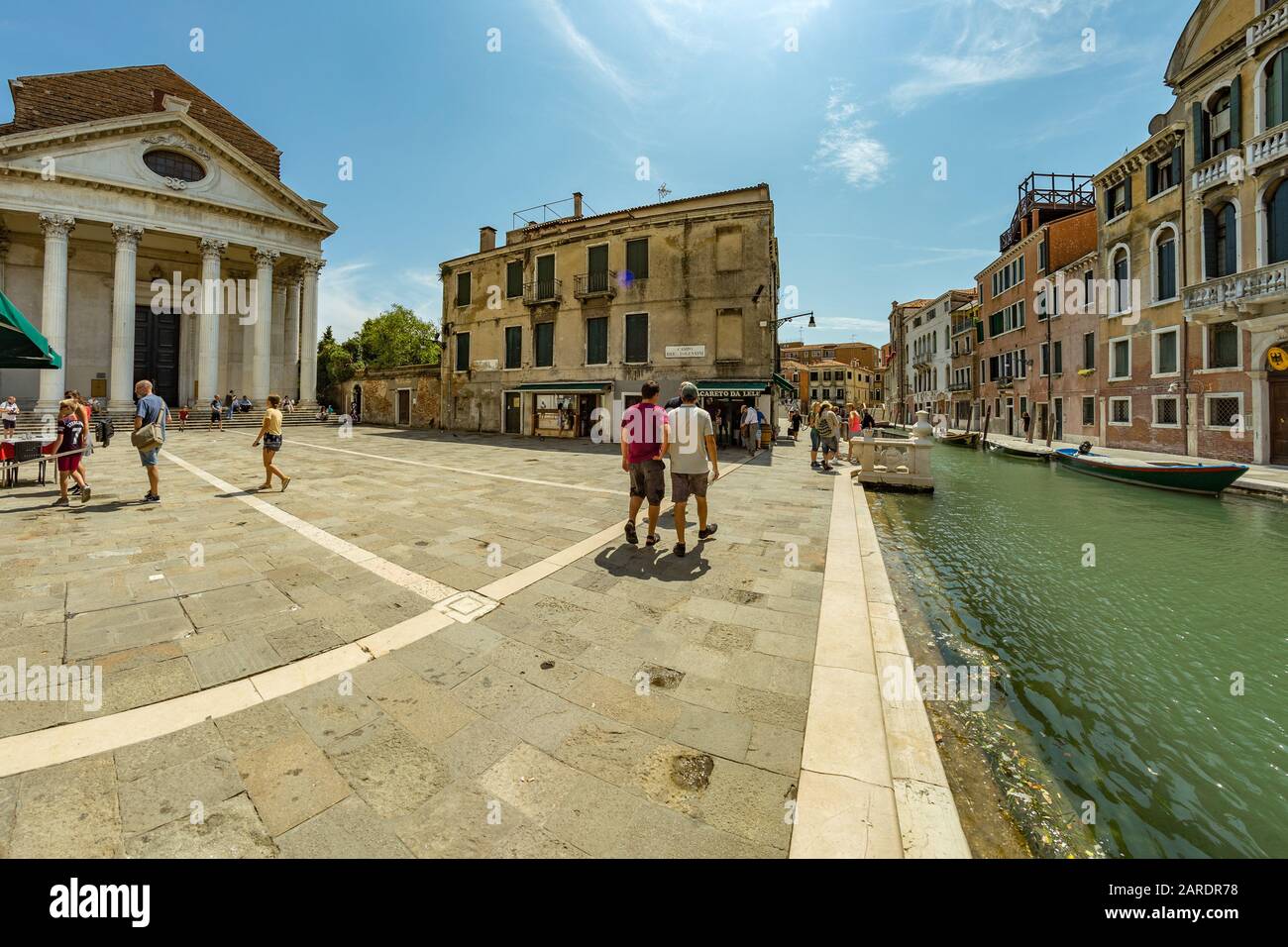 Venezia, Italia - 02 agosto 2019: uno delle migliaia di incantevoli angoli accoglienti a Venezia in una limpida giornata di sole. La gente del posto e i turisti passeggiano lungo il h Foto Stock