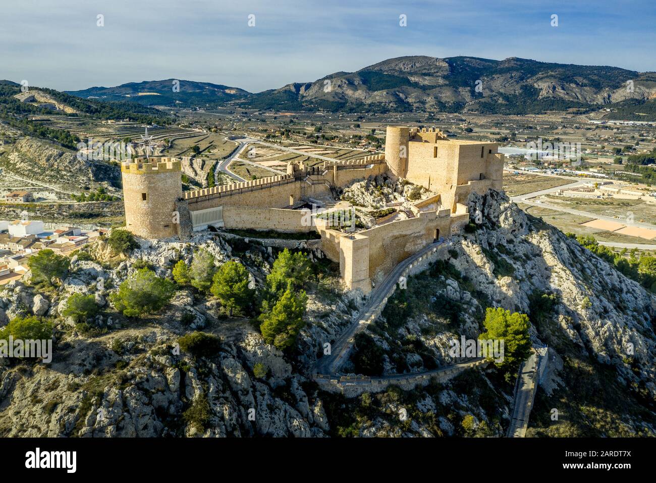 Veduta aerea del castello di Castalla, nella provincia di Valencia, Spagna, con il suo mastio che domina la città e un cortile rinforzato da una torre circolare al sole Foto Stock