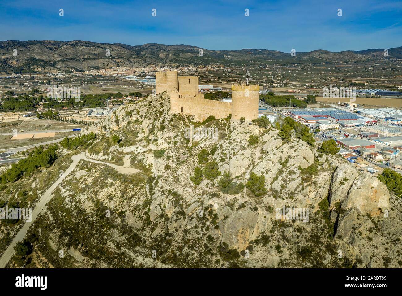 Veduta aerea del castello di Castalla, nella provincia di Valencia, Spagna, con il suo mastio che domina la città e un cortile rinforzato da una torre circolare al sole Foto Stock