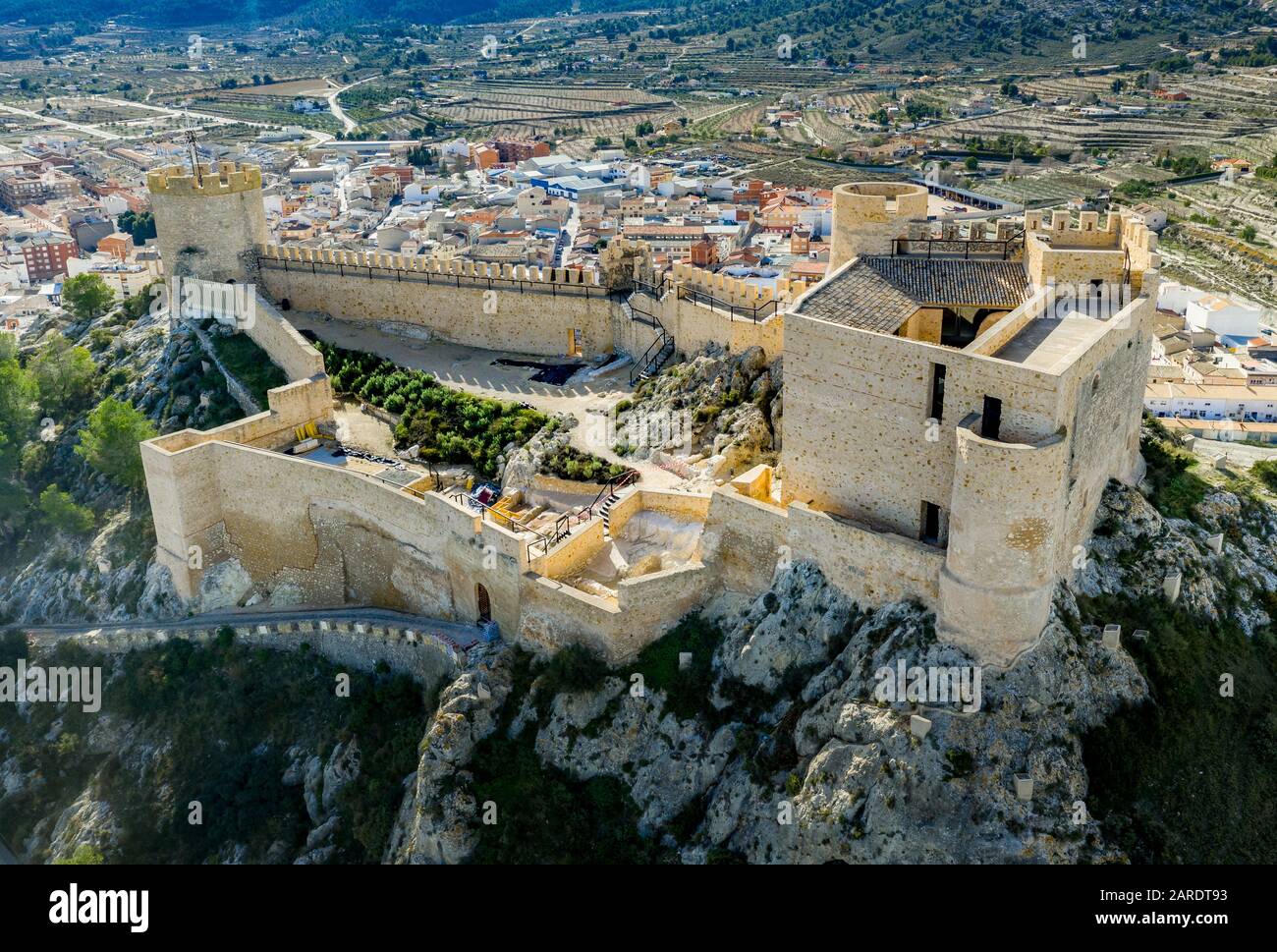 Veduta aerea del castello di Castalla, nella provincia di Valencia, Spagna, con il suo mastio che domina la città e un cortile rinforzato da una torre circolare al sole Foto Stock