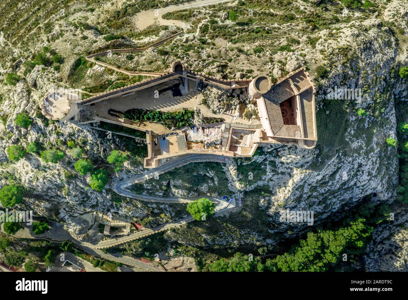 Veduta aerea del castello di Castalla, nella provincia di Valencia, Spagna, con il suo mastio che domina la città e un cortile rinforzato da una torre circolare al sole Foto Stock