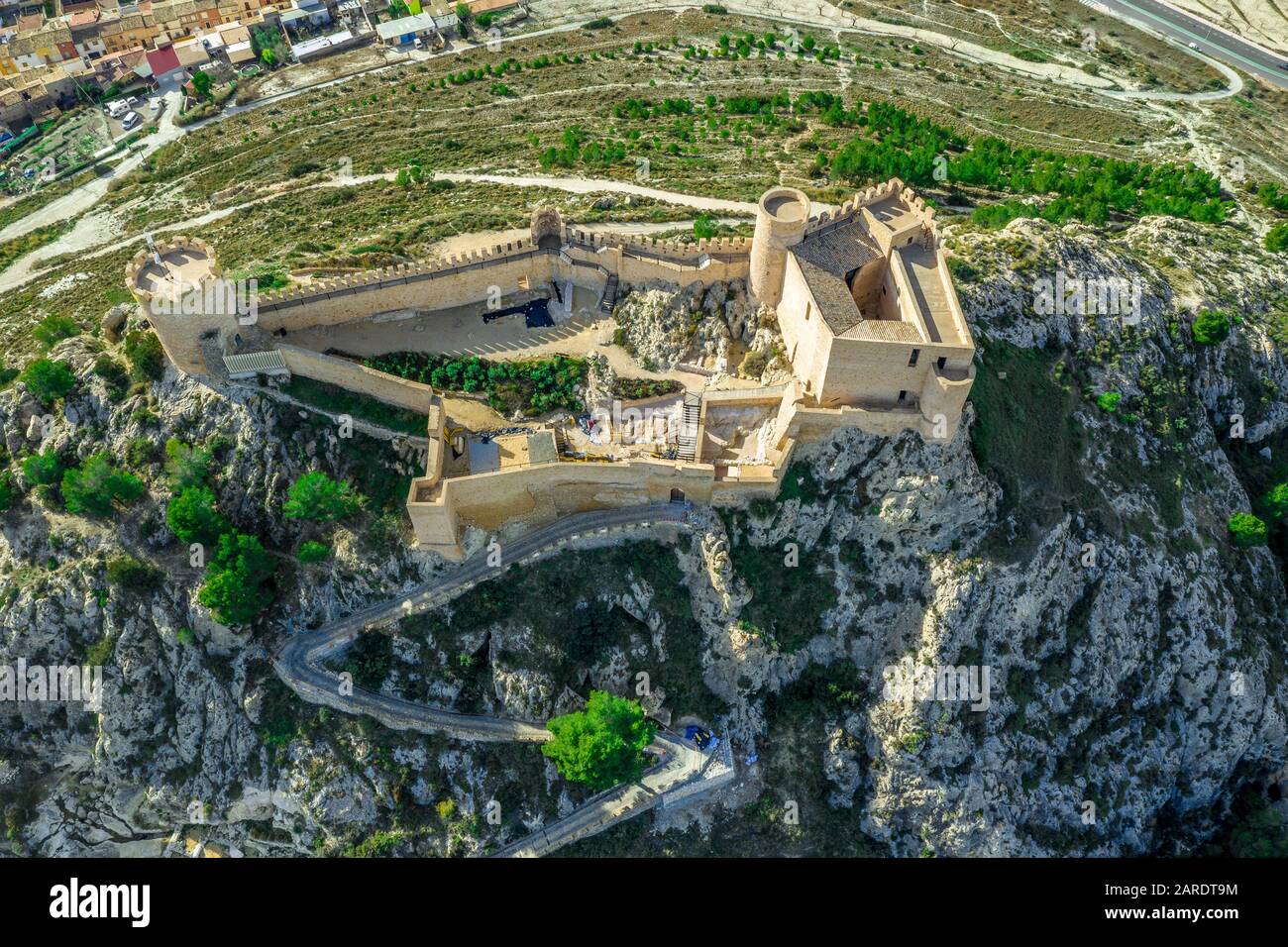 Veduta aerea del castello di Castalla, nella provincia di Valencia, Spagna, con il suo mastio che domina la città e un cortile rinforzato da una torre circolare al sole Foto Stock