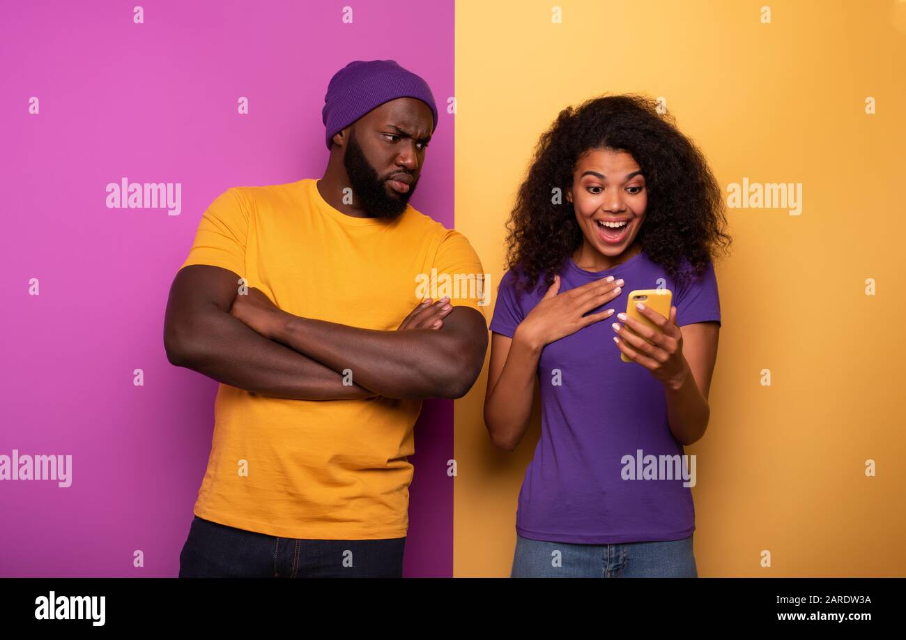 Ragazza ricevere un sacco di focolari sul sociale e del ragazzo è geloso su di esso. Giallo e viola sullo sfondo Foto Stock