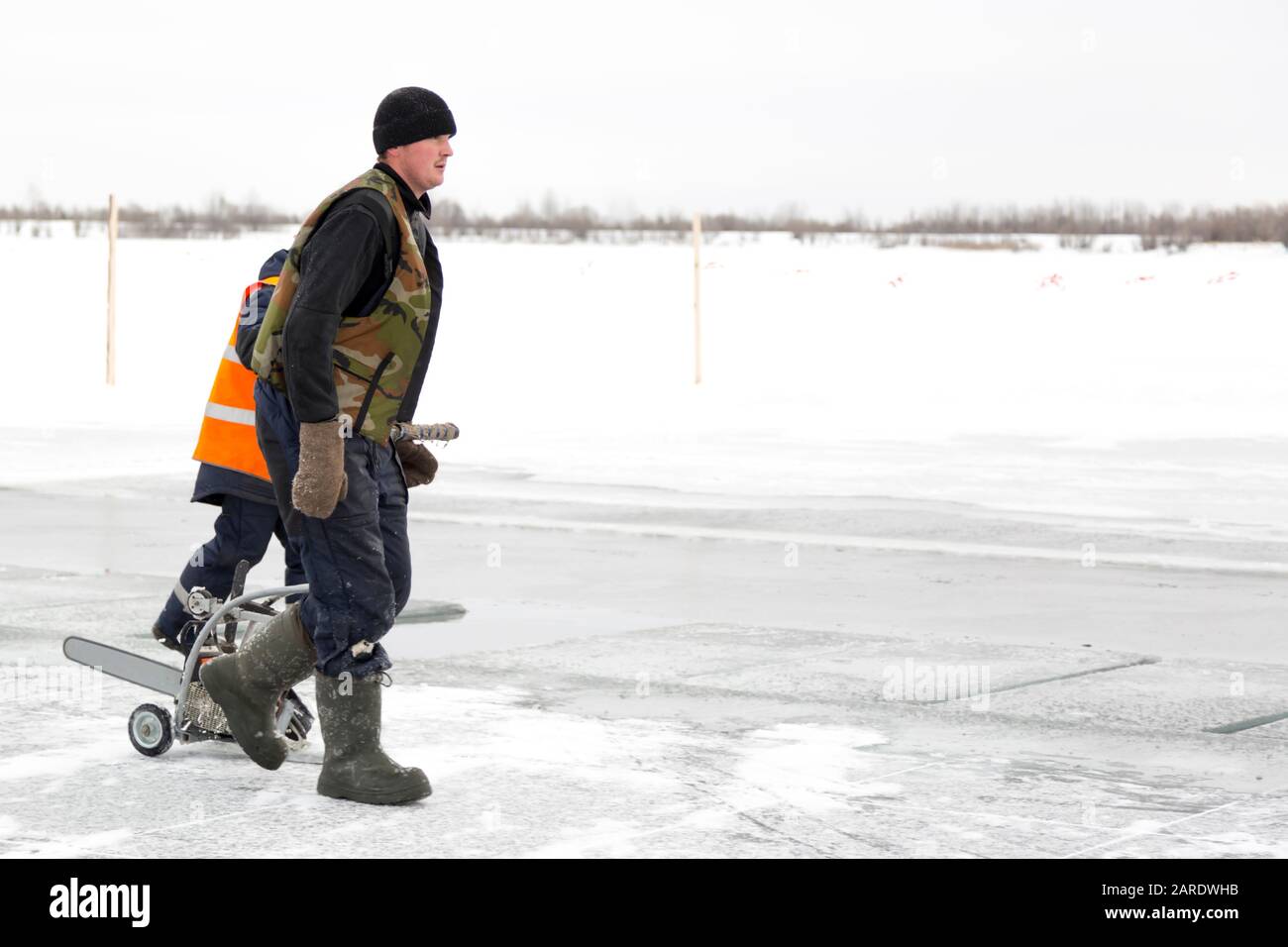 Un operaio cammina sul ghiaccio di un lago ghiacciato, con una macchina da taglio Foto Stock