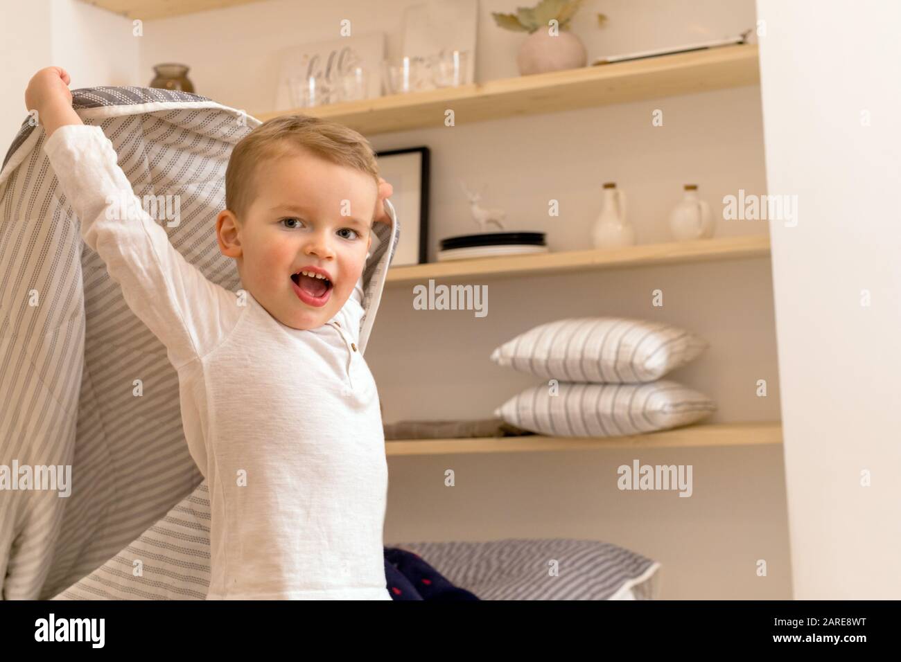 Il ragazzino soddisfatto gioca con la coperta a casa Foto Stock