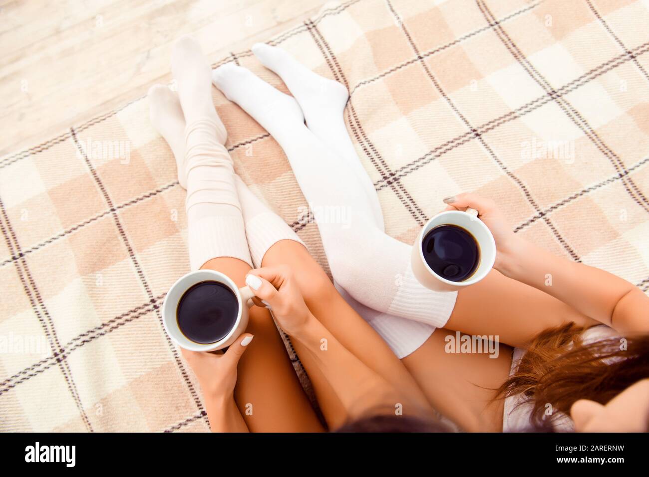 Vista dall'alto delle belle gambe femminili in calze bianche con tazze di caffè Foto Stock