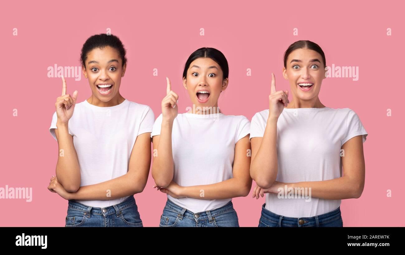Tre Millennial Girls Pointing Finger Up Standing, Pink Background, Panorama Foto Stock