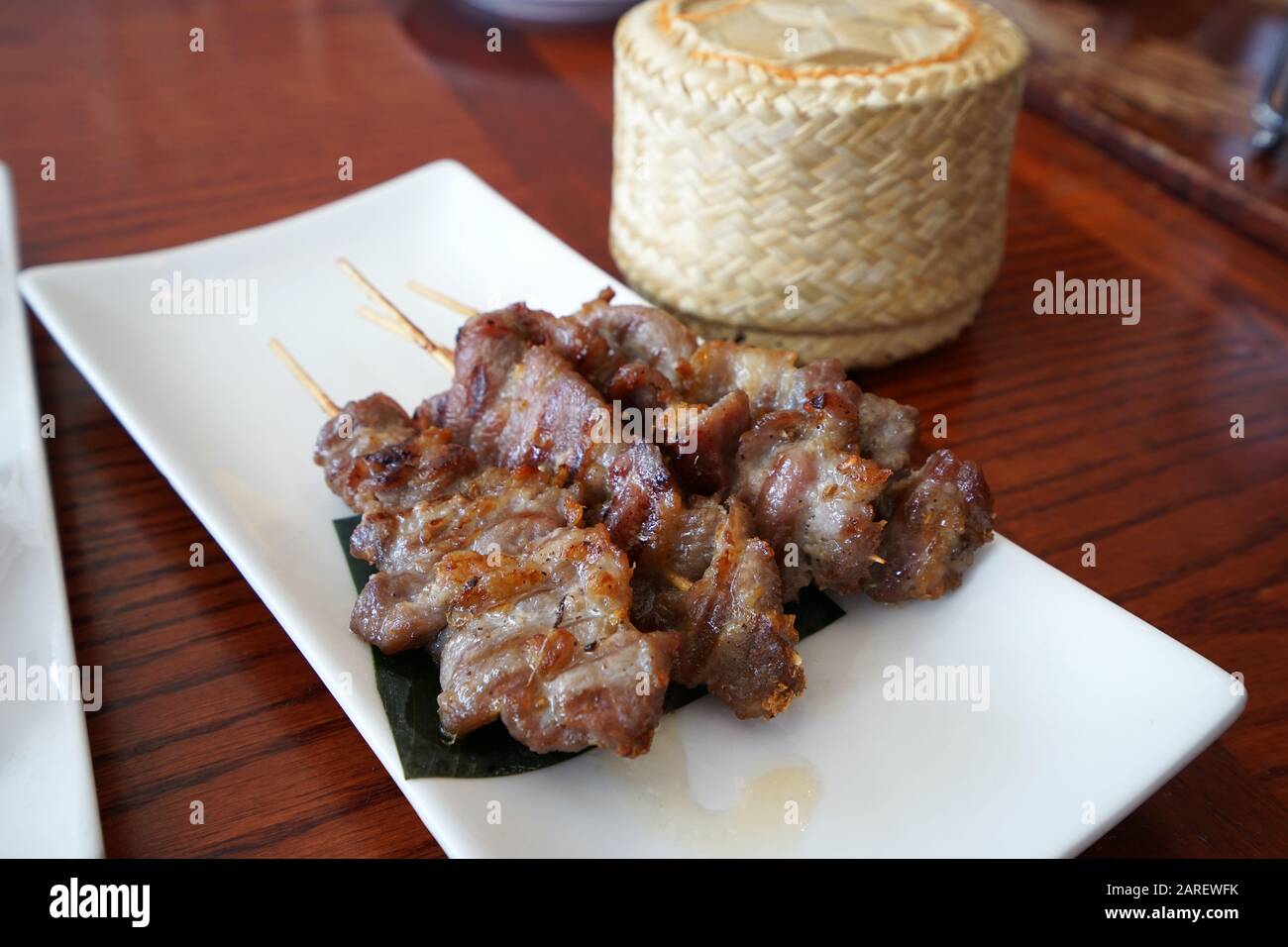 Spiedini di maiale barbecue serviti con un cesto di legno di riso appiccicoso, ricetta tailandese Foto Stock