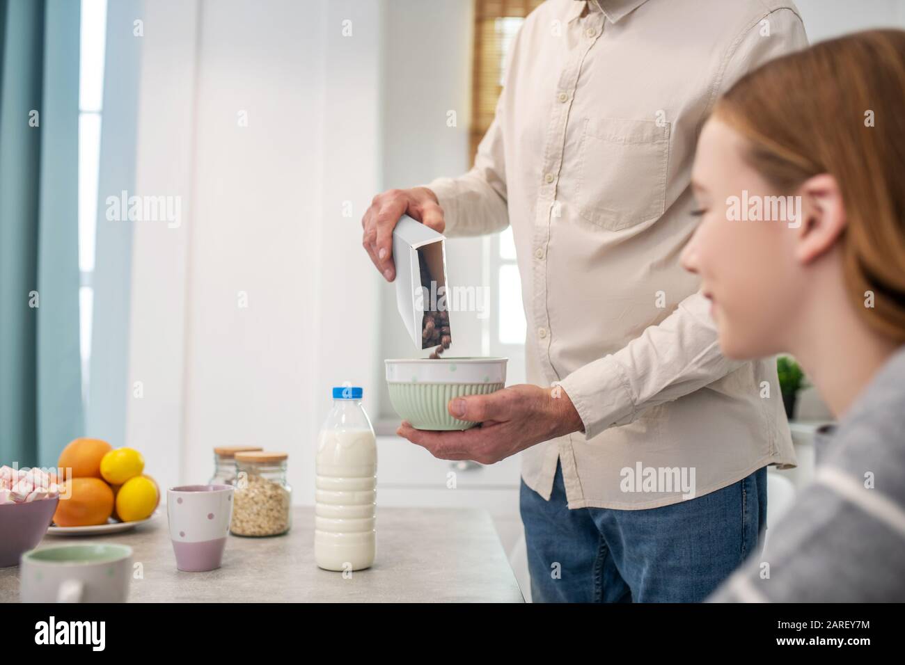 Figlia che guarda piatto con la granola nelle mani dei suoi padri. Foto Stock