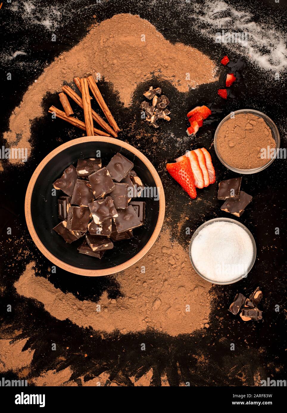 ciotola di pezzi di cioccolato ciotola di zucchero e cacao con pezzi di fragole e cannella, su uno sfondo nero Foto Stock