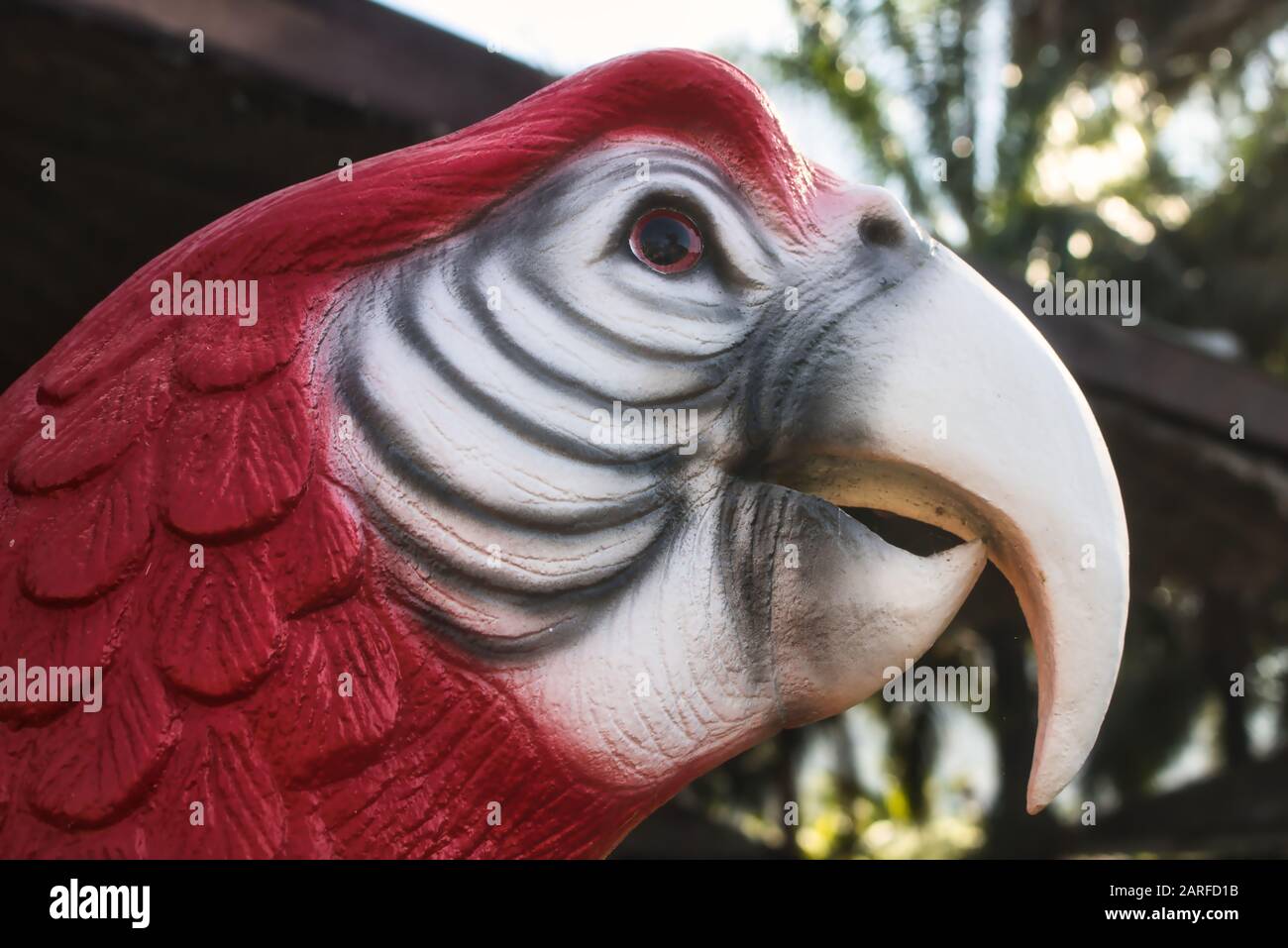 Questa foto unica mostra una testa di una statua di pappagallo in rosso e bianco in piedi in un giardino. Potete vedere i dettagli molto bene. Foto Stock