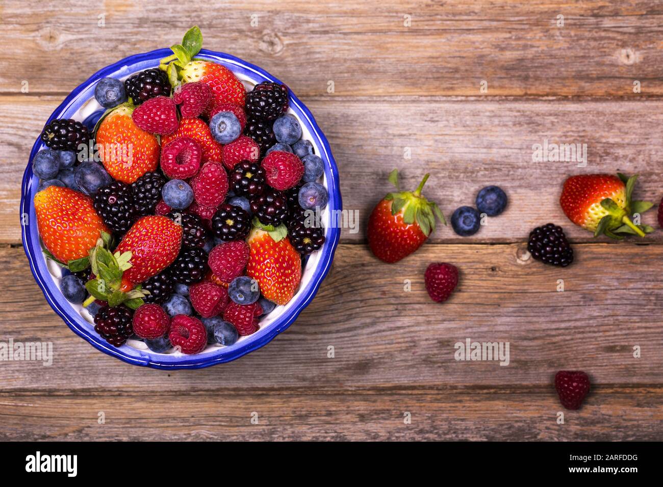 Vista dall'alto di una ciotola di frutta estiva, composta da fragole, lamponi, mirtilli e more, su un vecchio sfondo di legno. Primo piano con la massima intelligenza Foto Stock