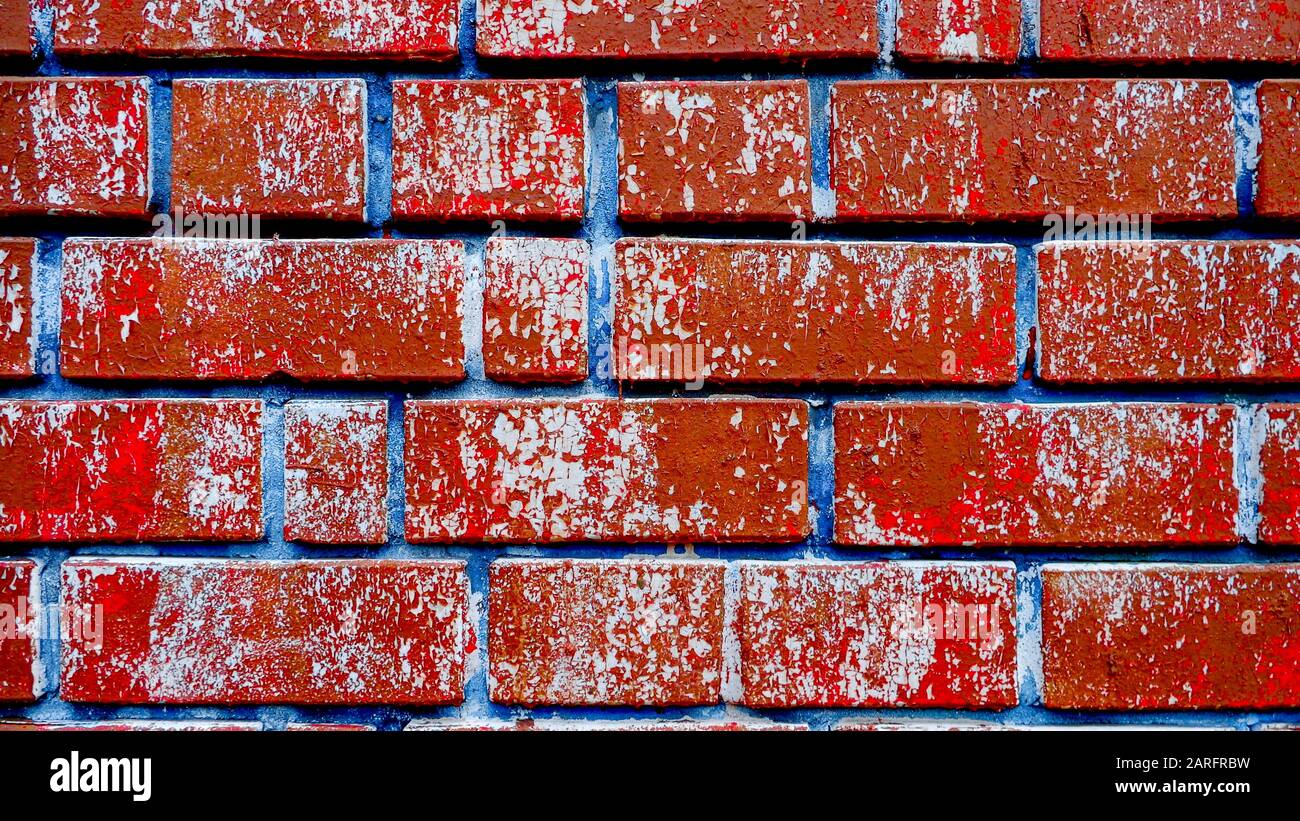 Parete in mattoni colorati con vernice rossastra fessurata e giunti blu, sfondo loft scuro Foto Stock