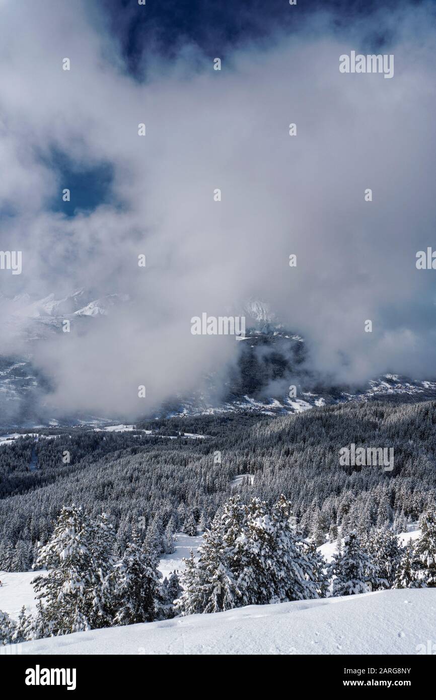 Bassa nube che soffia lungo la valle su alberi di pino innevato nella stazione sciistica francese di Meribel Foto Stock