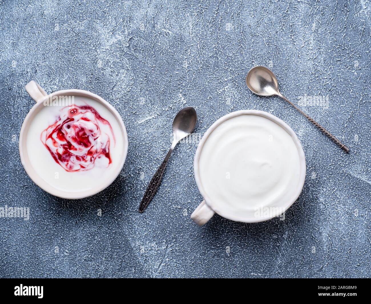 Due yogurt greco in ciotola bianca su un tavolo grigio in cemento blu, vista dall'alto Foto Stock