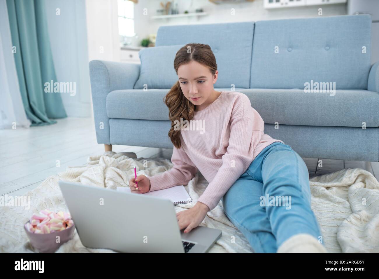 Ragazza che guarda un computer portatile sdraiato sul pavimento e disegno. Foto Stock