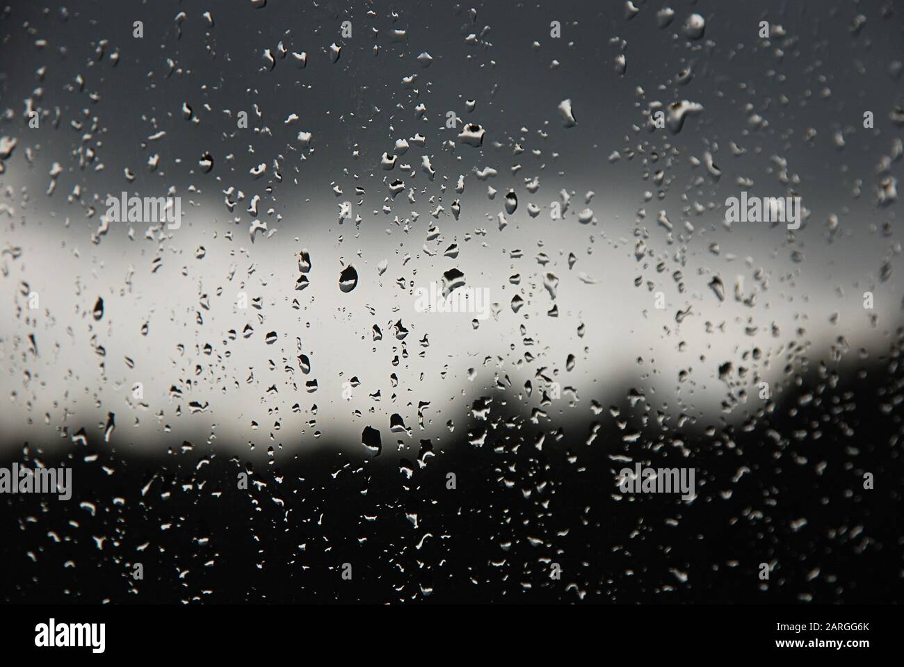 Gocce di pioggia nel riquadro della finestra. Sfumatura in bianco, grigio e nero su sfondo sfocato. Pioggia nuvoloso fuori dalla finestra. Raffreddamento, pioggia, maltempo Foto Stock