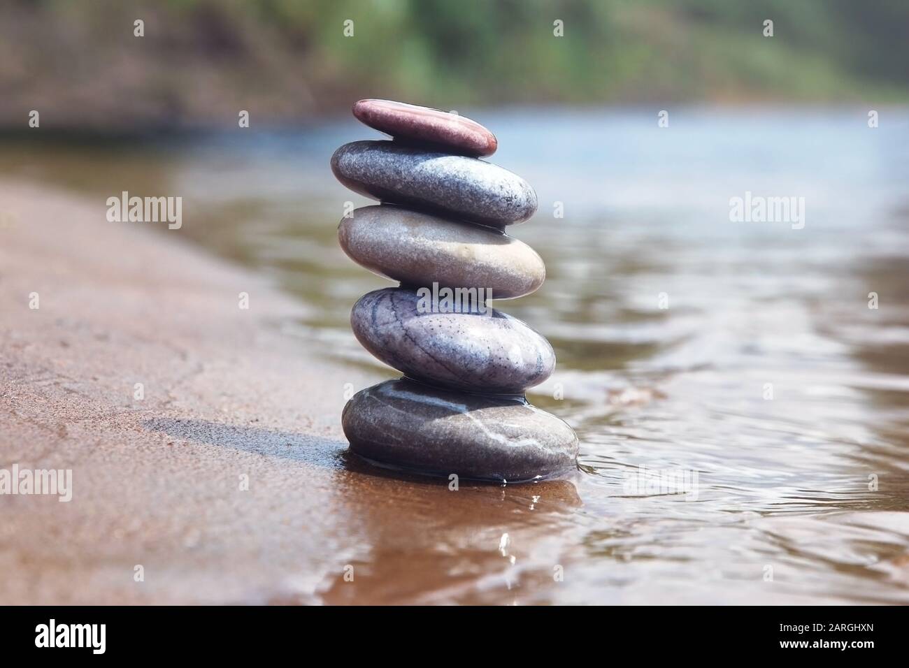 Pila di pietre di ghiaia equilibranti sulla sabbia e bordo di acqua. Simbolo Zen contro sfondo natura sfocata. Foto Stock