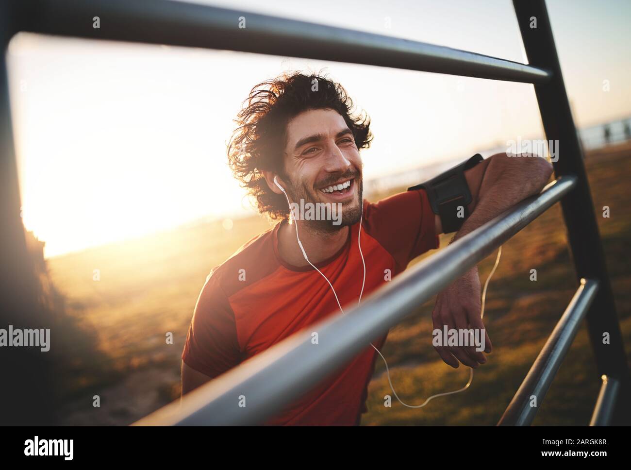Felice fit giovane corridore maschile godendo di ascoltare la musica sulle cuffie durante la luce del mattino Foto Stock