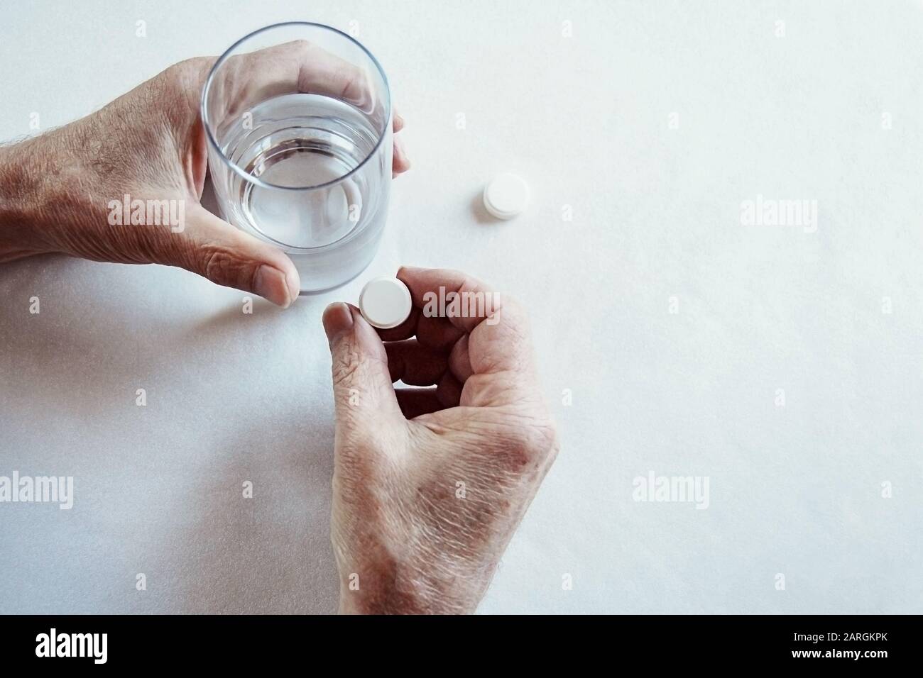 Le mani degli anziani che prendono la pillola della medicina con un vetro di acqua Foto Stock