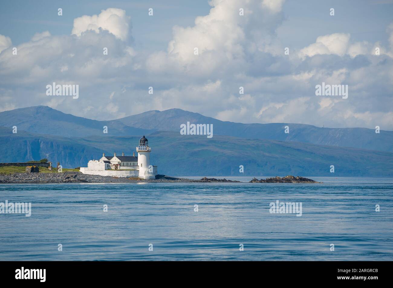 Seascape con faro e gamma di montani lontano. Isole Hebrides, Scozia. Foto Stock