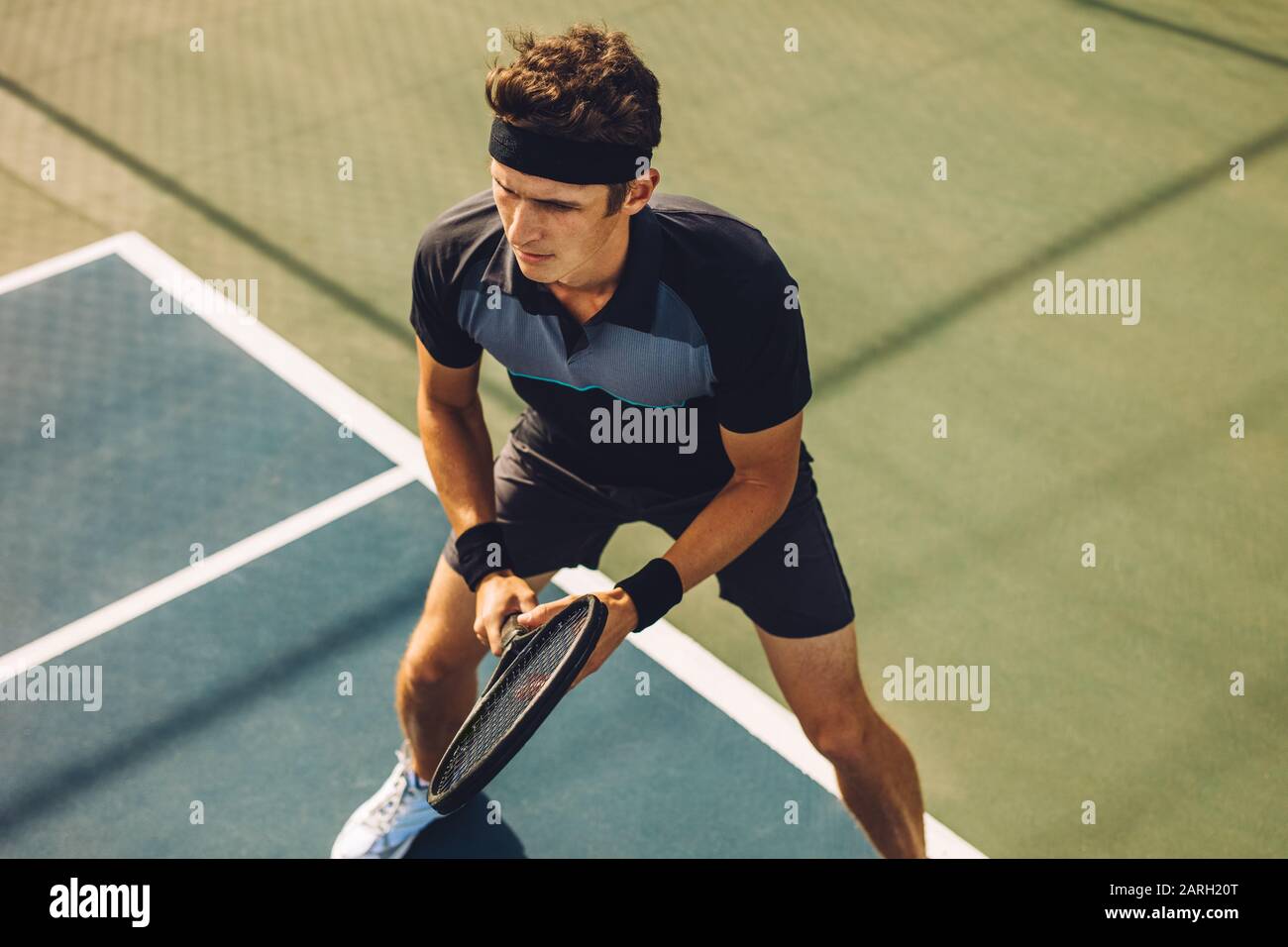 Giocatore di tennis professionista che gioca una partita sul campo duro. Sportivo caucasico in piedi sulla linea di base pronto a colpire la palla sul campo da tennis. Foto Stock