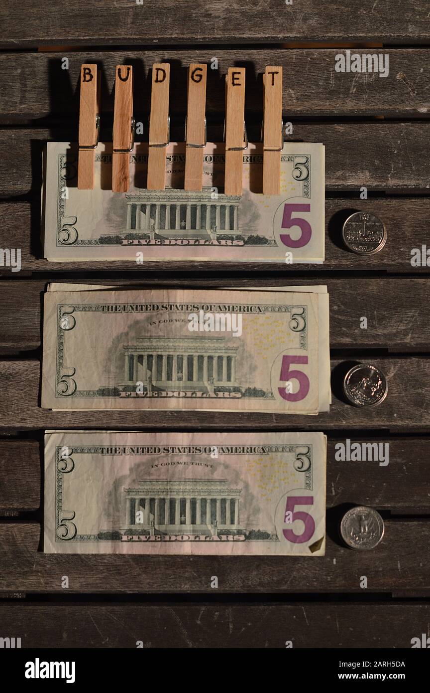 Pile di banconote e monete in dollari su un tavolo e clip con le lettere DI BILANCIO bruciato in loro su uno degli stack Foto Stock