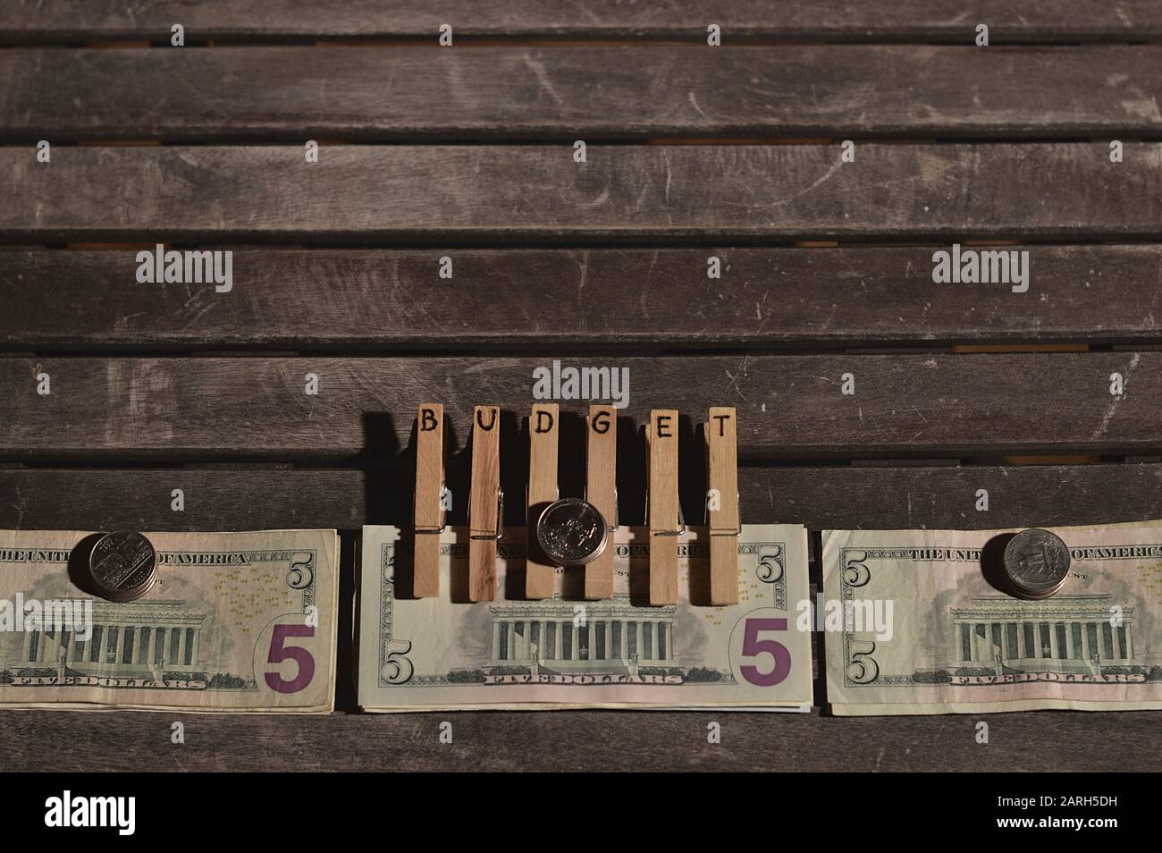 Pile di banconote e monete in dollari su un tavolo e clip con le lettere DI BILANCIO bruciato in loro su uno degli stack Foto Stock