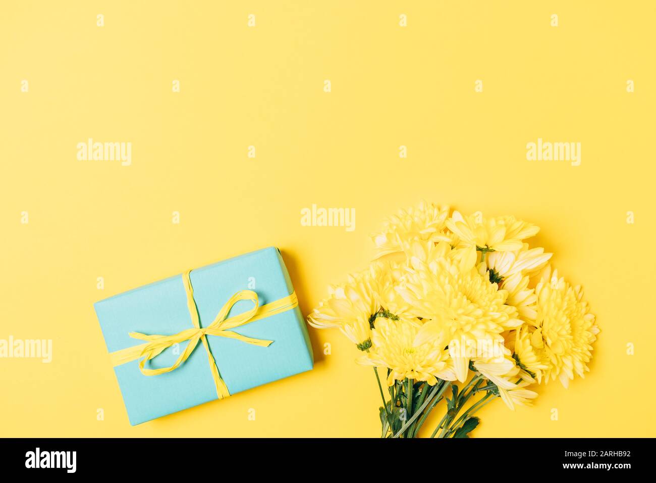 Auguri di vacanza piatto composizione confezione regalo e bouquet di fiori freschi su sfondo giallo. Foto Stock