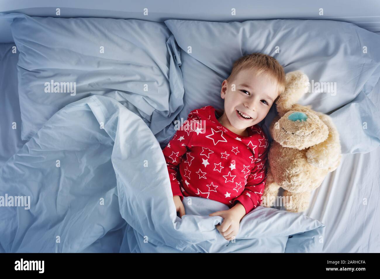 Ragazzo assonnato sdraiato a letto con lenzuola bianche Foto Stock