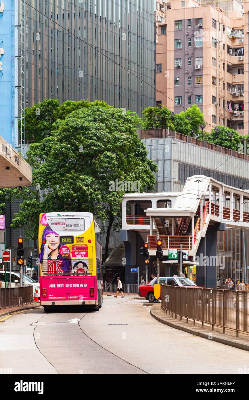 Hong Kong - 21 luglio 2017: L'autobus rosso passa per la strada nel quartiere centrale di Hong Kong, la gente comune e i turisti camminano per la strada. Foto verticale Foto Stock