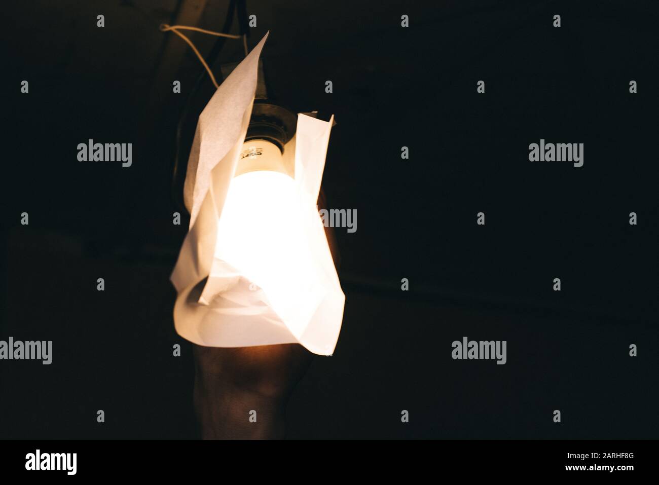 Un uomo avvolge la carta con una lampada elettrica. Violazione delle norme di sicurezza e di tutela del lavoro. Un lavoratore prende una lampadina con un'ite combustibile Foto Stock