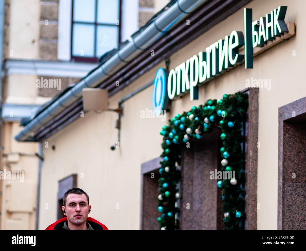 Mosca, Russia - 17 gennaio 2020: L'uomo vicino a Otkritie Bank firma sopra l'entrata. Garland di Natale di giocattoli di Natale e rami di abete intorno Foto Stock