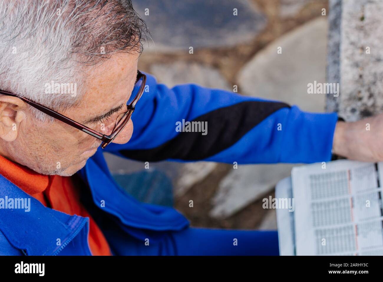 Uomo anziano con occhiali che legge il giornale nel parco con il pavimento sullo sfondo Foto Stock