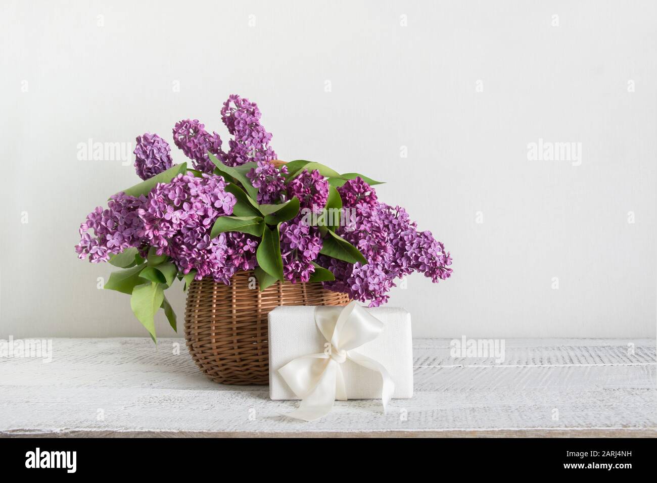 Cestino di fiori lilla in regalo su sfondo bianco di legno. Madri e donne giorno. Spazio per il testo. Orientamento orizzontale. Foto Stock