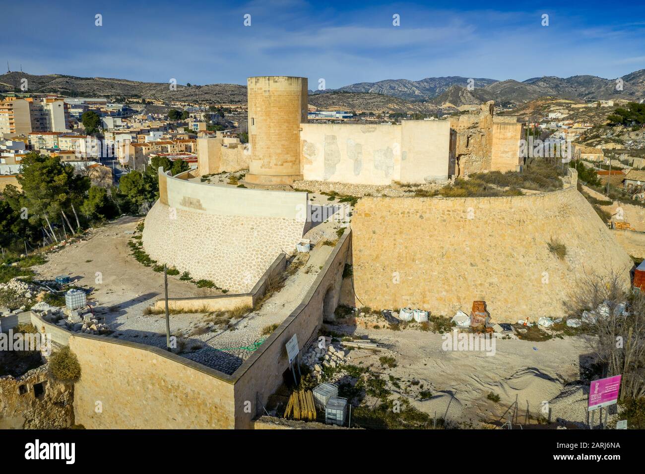 Veduta panoramica aerea del castello medievale di Elda sopra la città con mura, torri e porte parzialmente restaurate in pietra calcarea bianca in Spagna Foto Stock