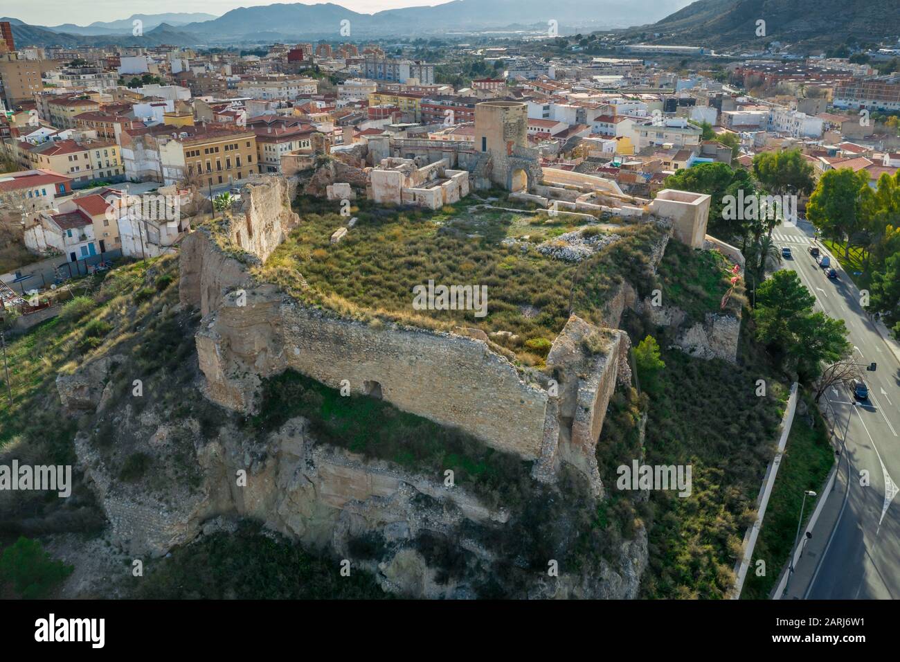 Veduta panoramica aerea del castello medievale di Elda sopra la città con mura, torri e porte parzialmente restaurate in pietra calcarea bianca in Spagna Foto Stock