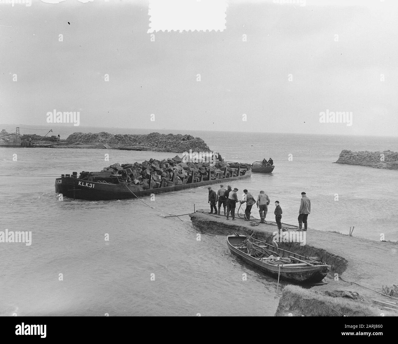 Watersnood 1953] Il buco della diga vicino a Herkingen op Goeree-Overflakkee, che è stato fatto all'inizio di febbraio 1953, ma non è stato chiuso nel tempo, è ora chiuso con blocchi di basalto. Chiatte soffitta con questi blocchi sono salpate nel buco, e a grande velocità i pezzi di basalto sono poi gettati nell'acqua. Date: 12 Marzo 1953 Location: Goeree-Overflakkee, Herkingen, Zuid-Holland Keywords: Restaurazioni, Inondazioni Foto Stock