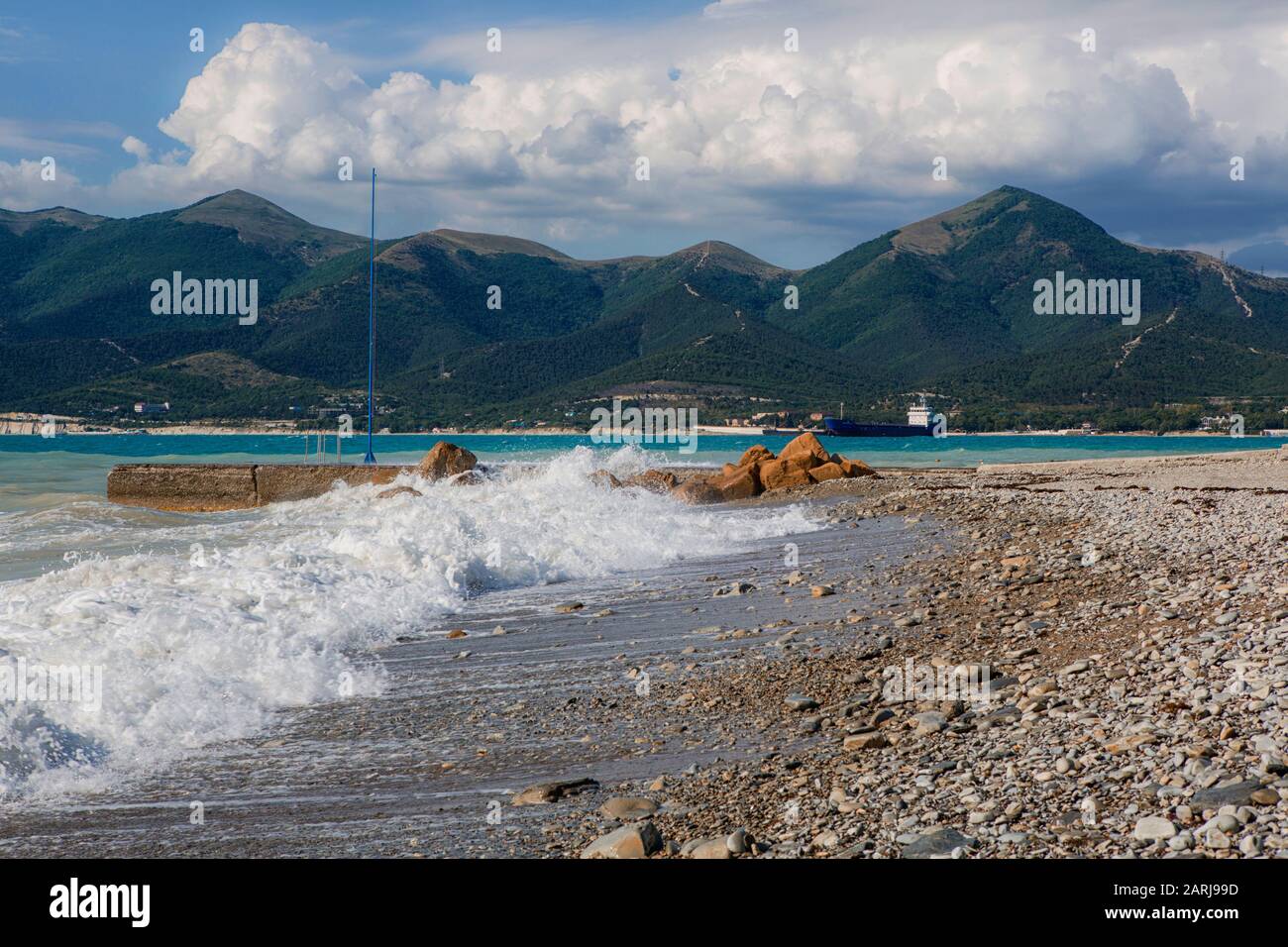 Spiaggia di ciottoli nella località di Kabardinka, regione Krasnodar, Mar Nero. Onde e surf su una spiaggia di ghiaia. All'orizzonte della montagna - Markoth ridg Foto Stock