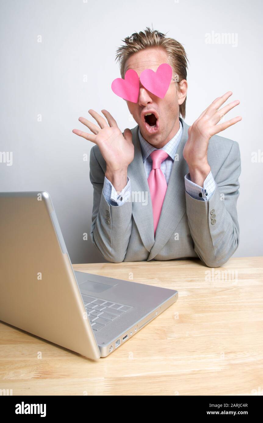Sorpreso lavoratore di ufficio guardando il suo computer portatile con cuori rosa fluttering sopra i suoi occhi Foto Stock