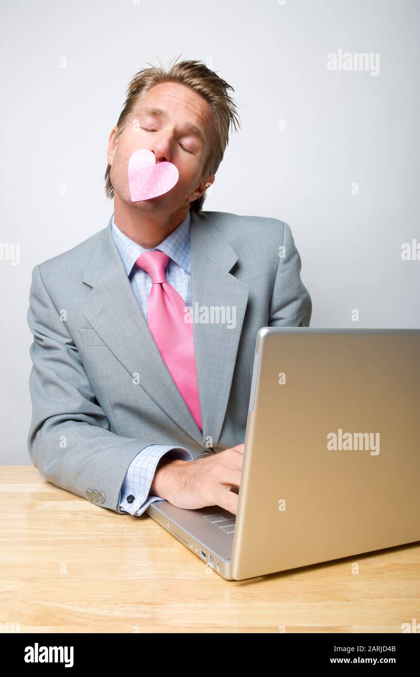 Uomo d'affari romantico seduto in ufficio dando un bacio di cuore rosa Foto Stock