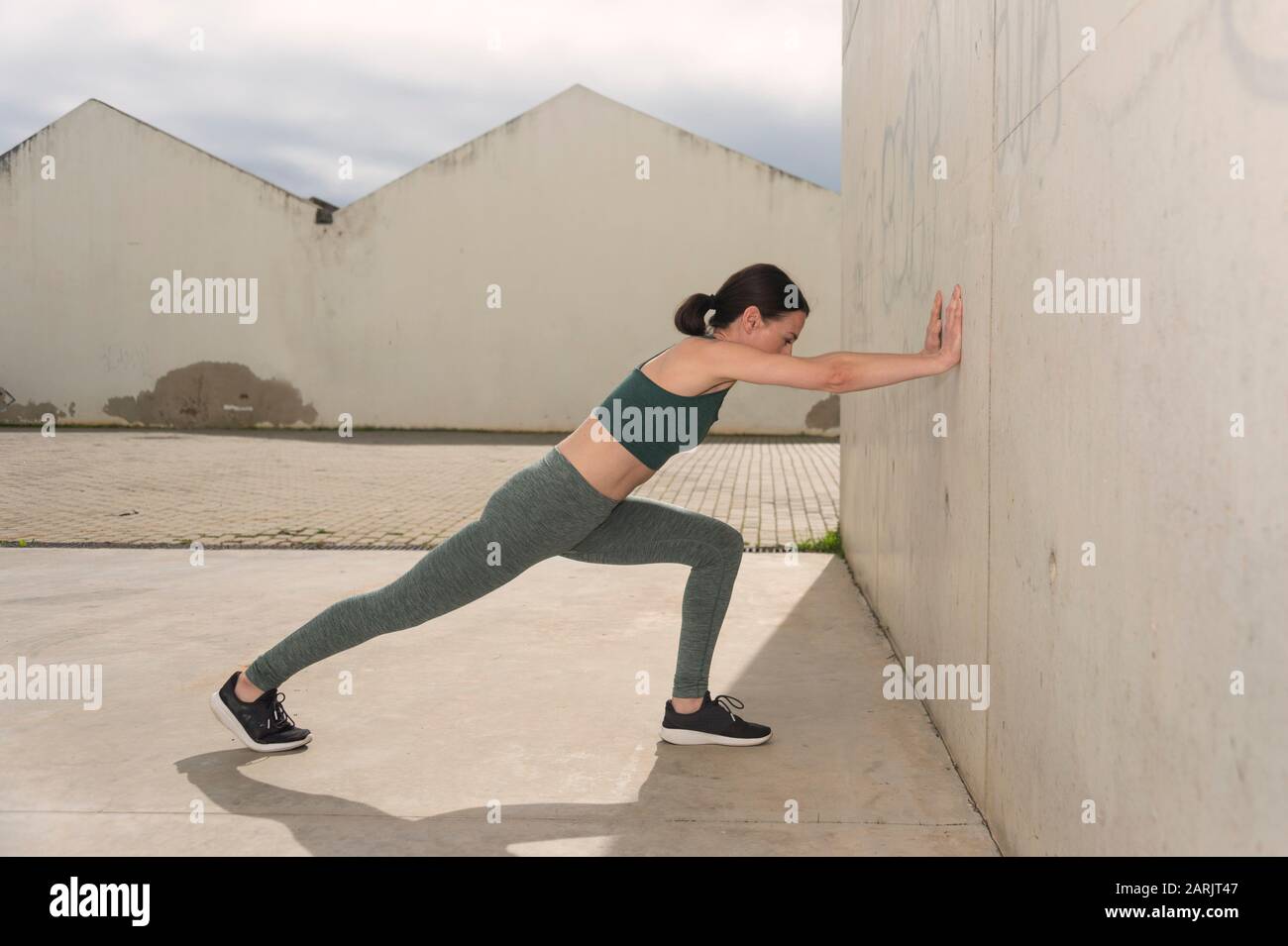sportswoman stretching braccia e gambe, esercizi di riscaldamento, ambiente urbano concreto. Foto Stock
