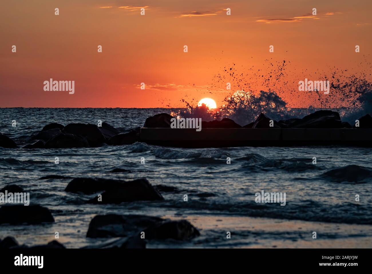 Il sole tramonta dietro le onde che si infrangono Foto Stock