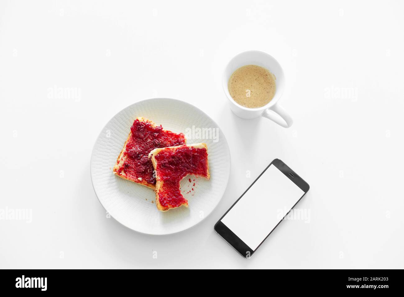 La colazione è a tavola. Una tazza di caffè e toast con marmellata di ciliegie accanto al telefono. Foto Stock