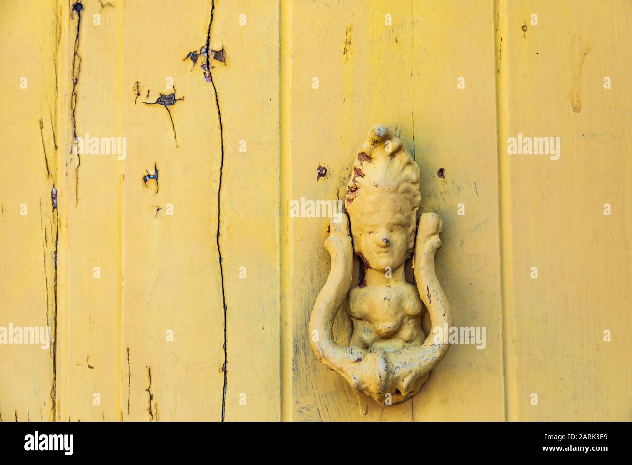 Italia, Sicilia, Provincia Di Messina, Novara Di Sicilia. Porta gialla in legno con un knocker a forma di persona, nella cittadina collinare medievale di Francavilla di si Foto Stock