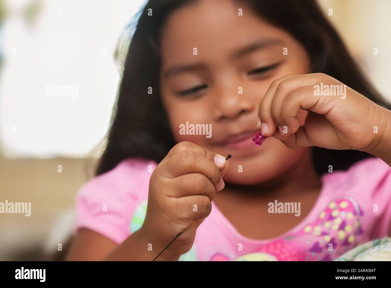 Una bambina carina che si diverte mentre si crea bead gioielli utilizzando stringa e perle colorate. Foto Stock
