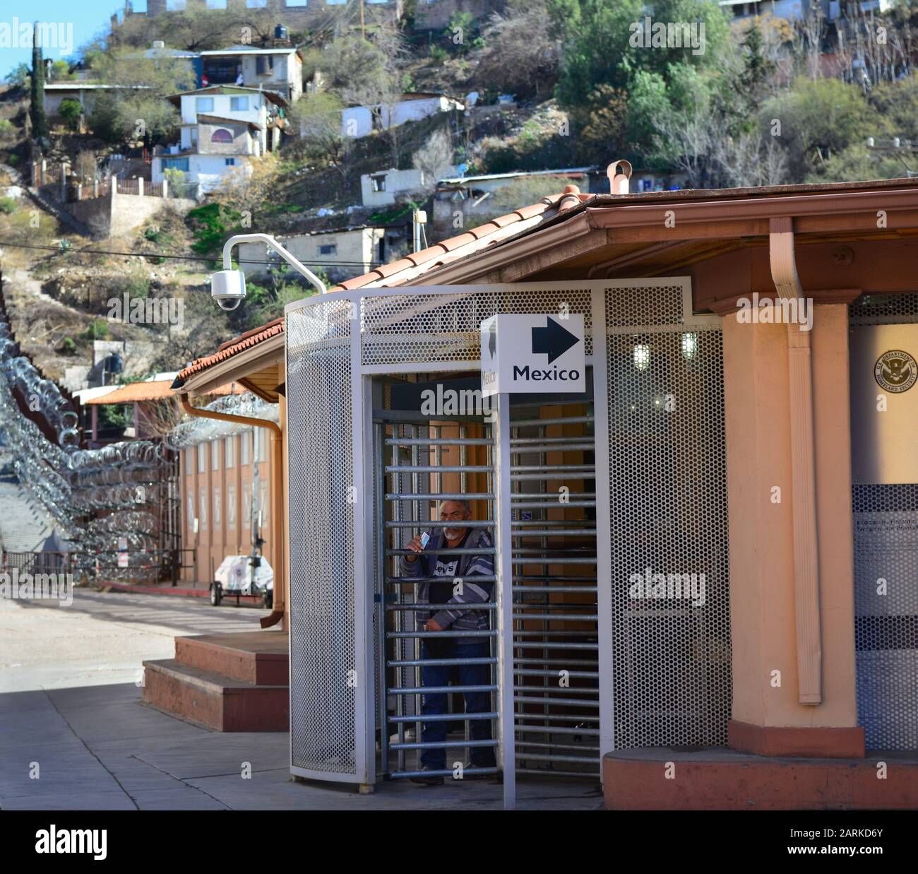 Persone che attraversano il confine USA/Messico a piedi al Punto Di Ingresso Al Confine con la porta Morley negli Stati Uniti con recinzione di confine e case messicane sullo sfondo Foto Stock